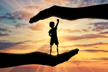 Help children with disabilities concept. Happy disabled boy with a prosthetic leg standing in the helping hands at sunsetの写真素材
