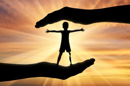 Help children with disabilities concept. Happy disabled boy with a prosthetic leg standing in the hands of human helpの写真素材