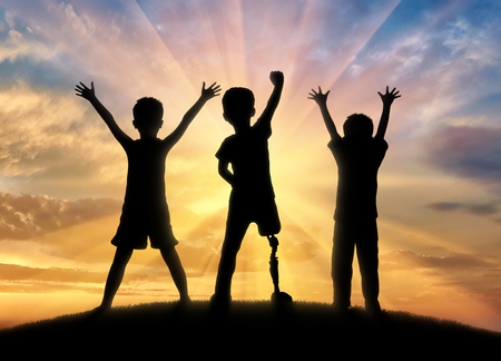 Childhood children with disabilities concept. Happy disabled boy with a prosthetic leg standing among his friends, on top of a hillの写真素材