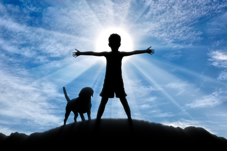 Happy childhood concept. Silhouette of a happy child on top of a hill at sunset with the dogの写真素材