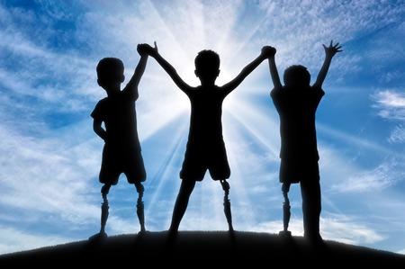 Children's disability concept. Children with disabilities with a prosthetic leg standing, holding hands against skyの写真素材