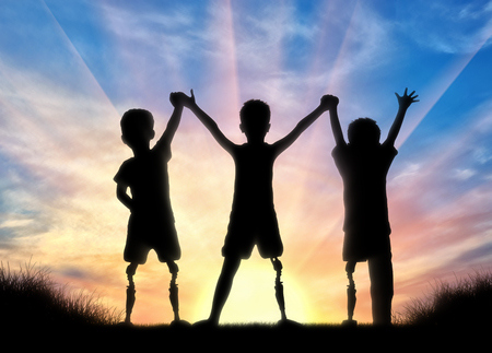 Children's disability concept. Happy children with disabilities with a prosthetic leg standing, holding hands on sunset backgroundの写真素材