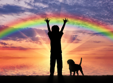 Happy childhood concept. Silhouette of a happy child and dog on the background of sea sunset and rainbowの写真素材