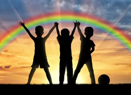 Childhood concept. Three happy children holding hands on a background of a rainbow at sunsetの写真素材