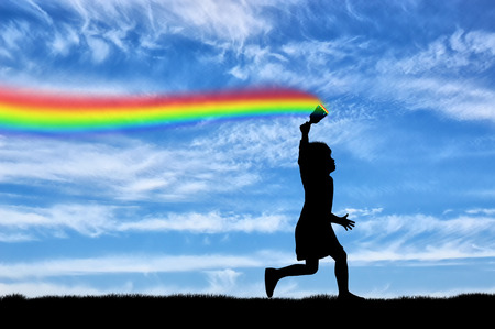 Childhood concept. The child with brush in hand, runs, and draws a rainbow in the skyの写真素材