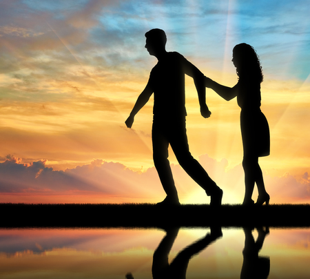 The concept of divorce and parting of a married couple. Silhouette of man throwing woman on sunset backgroundの写真素材