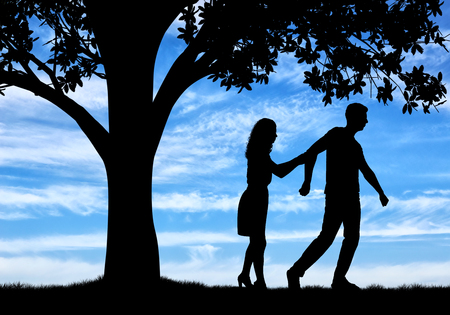 The concept of divorce and parting of a married couple. Silhouette of a man throwing a woman near a treeの写真素材