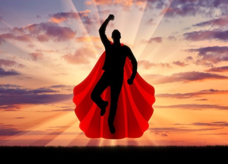Superman businessman superhero. Silhouette of a businessman in the image of a superman flies in the sky at sunsetの写真素材