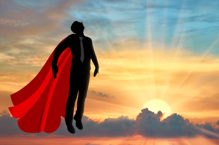 Superman businessman superhero. Silhouette of a businessman in the image of a superman flies in the sky at sunsetの写真素材