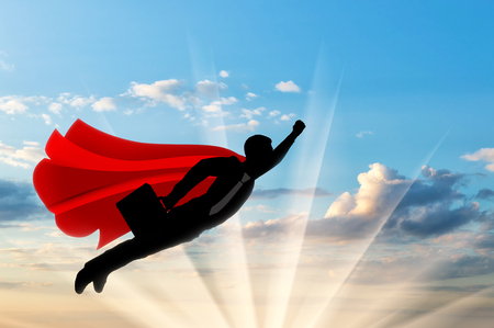 Superman businessman superhero. Silhouette of a businessman in the image of a superman flies in the sky with a briefcase on dawnの写真素材