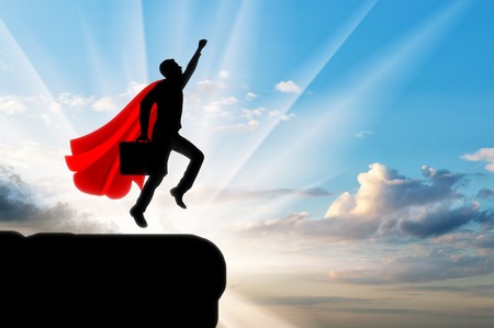 Superman businessman superhero. Silhouette of a businessman in the image of a superman flies in the sky with a briefcase on dawnの写真素材