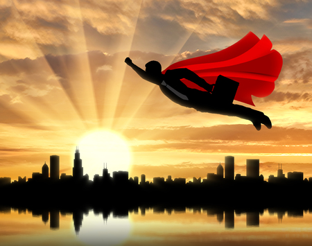 Superman businessman superhero. Silhouette of a superman businessman with a briefcase flying in the sky over the city at sunsetの写真素材