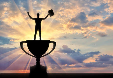 The concept of leadership in business. Silhouette of a businessman standing on the trophy at sunsetの写真素材