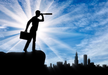 The concept of motivated businessman. Silhouette of a businessman looking through a telescope to the city in search of new opportunitiesの写真素材