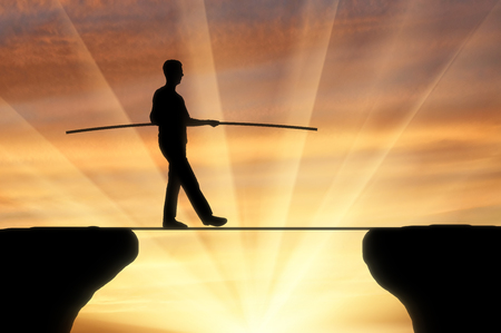 The concept of balance in business. Silhouette of businessman walking, on the tight rope at sunsetの写真素材