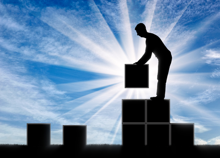 The concept of growth in business. Silhouette of a businessman who builds stairs up from square blocksの写真素材