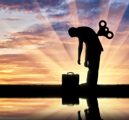 The concept tired businessman. Silhouette tired businessman with a clockwork mechanism on the backの写真素材