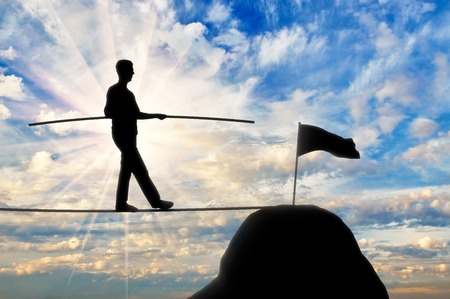 The concept of balance and equilibrium in the business. Silhouette of a businessman walking toward the target on the tight ropeの写真素材