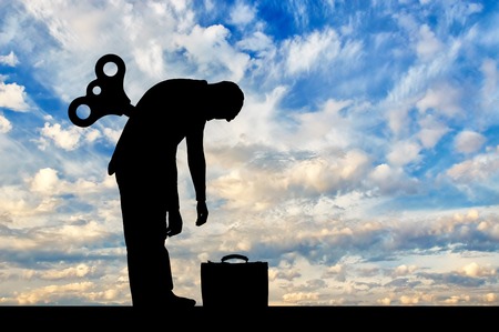 The concept tired businessman. Silhouette tired businessman with a clockwork mechanism on the backの写真素材