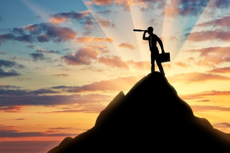 The concept of purposeful businessman. Silhouette of a businessman looking through a telescope on top of a mountain in search of new opportunitiesの写真素材