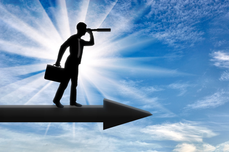 A silhouette of a businessman looking through a telescope into the distance while standing on the arrow. Business opportunity conceptの写真素材