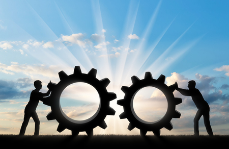 Silhouette of two people who want to connect the two gears in a single mechanism. The business partnership conceptの写真素材