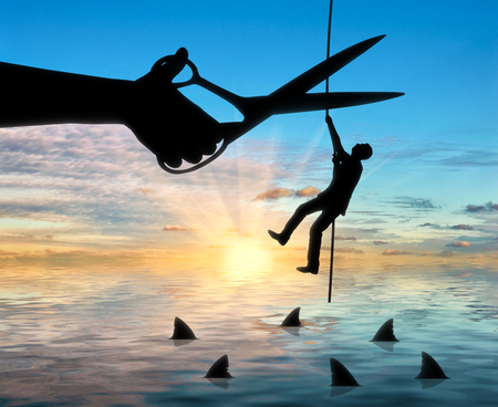 Silhouette of a businessman climbs a rope above the sharks and a hand with scissors intends to cut the rope. The concept of competition and risks in businessの写真素材