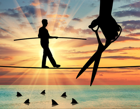 Silhouette of a businessman walking on a rope balancing, under it sharks, a hand with scissors intends to cut the rope. Concept of risks and dangers in businessの写真素材