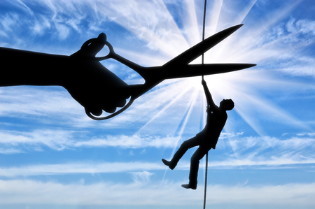 Silhouette of a businessman climbs on a tightrope and a hand with scissors intends to cut a rope. The concept of a rival in businessの写真素材