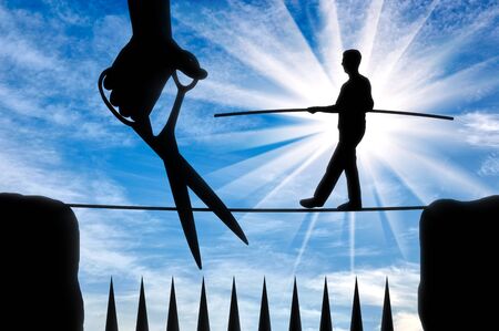 Silhouette of a man balances on a rope over sharp spikes and a hand with scissors intends to prune a rope. Concept of risks in businessの写真素材