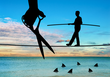 Hand with scissors intending to cut the rope where the businessman is teetering over the sharks. The concept of competition and risk in businessの写真素材