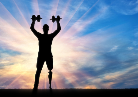 A man with a prosthetic leg standing with dumbbells in hand. The concept of persons with disabilities in sportsの写真素材