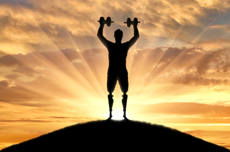A man with a prosthetic leg standing with dumbbells in hand. The concept of disabled people in sportの写真素材