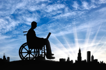 A disabled person in a wheelchair working with a laptop in hand on background of the city. The concept of the opportunity to work for people with disabilitiesの写真素材
