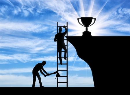 A business rival cuts a ladder on which another person climbs to the trophy. The concept of envy of the opponent to the success of another personの写真素材