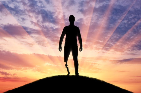 A man with a prosthetic leg standing on the sunset. The concept of prosthetic legs and rehabilitationの写真素材