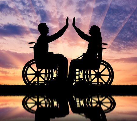 Silhouette of a woman and a man in a wheelchair, support each other and their reflection in the water. The concept of mutual aid people with disabilitiesの写真素材