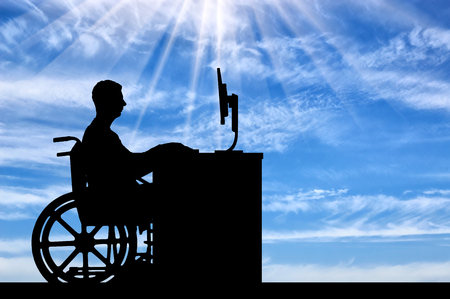 The employee is a disabled man in a wheelchair sitting behind a Desk with a computer . The concept of employment of persons with disabilitiesの写真素材