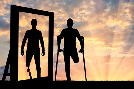 Silhouette of a man with an amputated leg sees a reflection of himself in the mirror with a prosthetic leg. The concept of the prosthetics of people with disabilitiesの写真素材