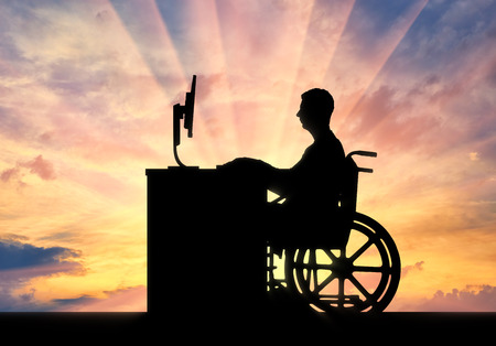 The employee is a disabled man in a wheelchair sitting behind a Desk with a computer on a sunset background. The concept of employment of persons with disabilitiesの写真素材