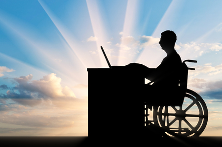 A disabled employee in a wheelchair working with a laptop at the table. The concept of employment of persons with disabilitiesの写真素材