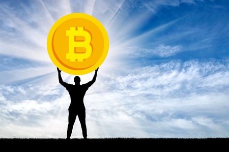 Silhouette of a man holding a coin bitcoin against the sky. The concept of the future for crypto currencyの写真素材