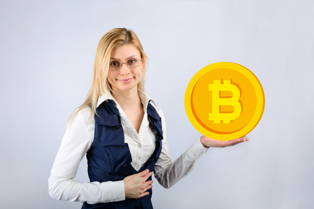 A woman in glasses holds a bitcoin in her hand. The concept of crypto currencyの写真素材