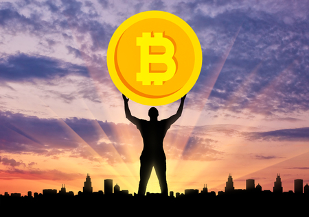 Silhouette of a man holding a coin bitcoin against the background of the city at sunset. The concept of the future for crypto currencyの写真素材