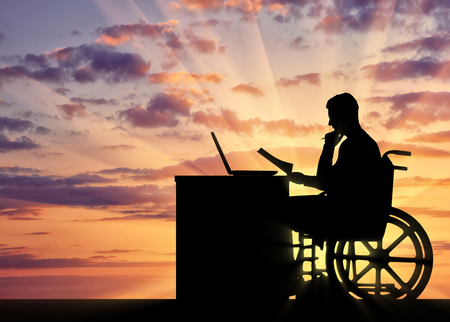 Silhouette of a man a businessman disabled in a wheelchair sitting at a table. The concept of working disabled peopleの写真素材