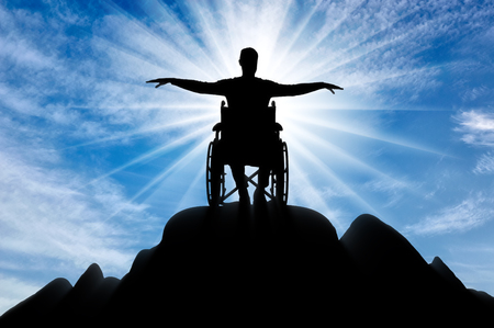 Silhouette of happy disabled man in wheelchair on top of mountain. The concept of happy people with disabilitiesの写真素材
