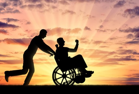 Silhouetted cheerful man having a disabled man in a wheelchair and his friend on a sunset background. Concept of people with disabilities in societyの写真素材