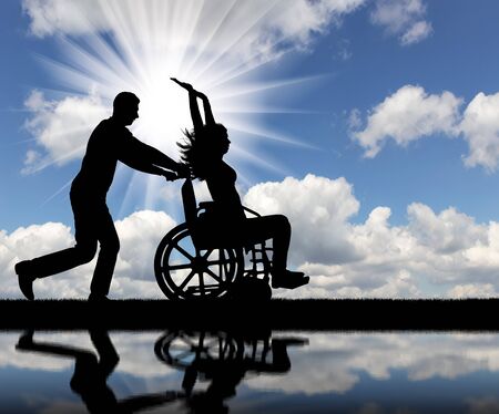 A fun time for a healthy man and a disabled woman in a wheelchair by the river. The concept of leisure for people with disabilitiesの写真素材