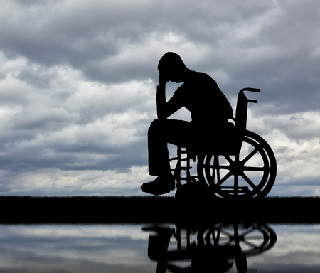 Silhouette of sad man crying in the disabled wheelchair. The concept of people with disabilities experiencing grief for the loss of healthの写真素材
