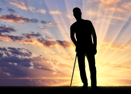 Silhouette of a disabled man supports himself with a crutch against the sunset background. Concept of people in rehabilitationの写真素材